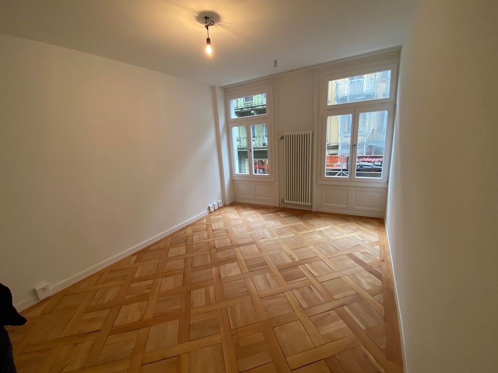 Helles leeres Zimmer mit Fischgrätparkett und großen Fenstern