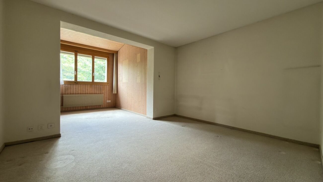 Leerer Wohnraum mit angrenzender Holzverkleidung und Fensterfront