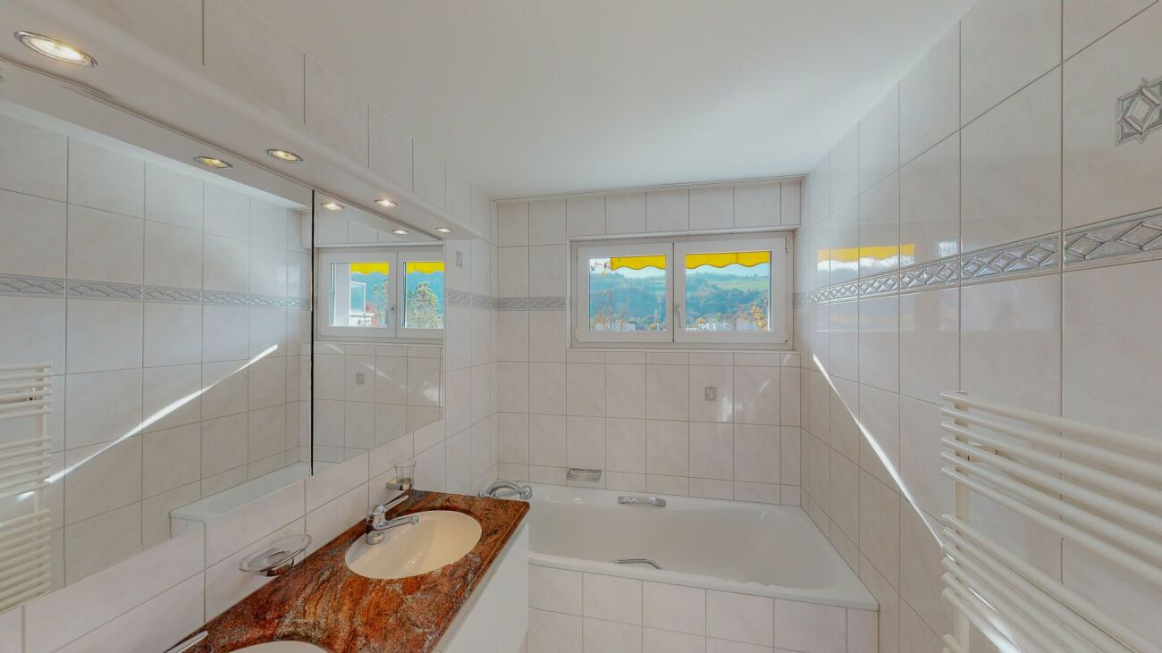 Helles Badezimmer mit Badewanne und Fensterblick