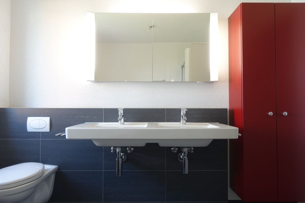 Modernes Badezimmer mit Doppelwaschbecken und rotem Hochschrank