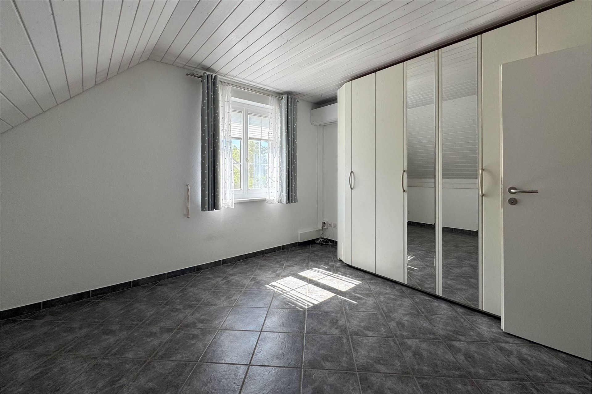 Helles Dachgeschosszimmer mit Fliesenboden und Kleiderschrank