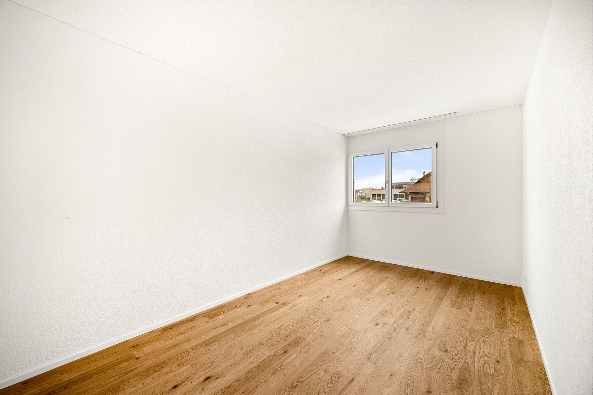 Helles, leeres Zimmer mit Parkettboden und Fensterblick