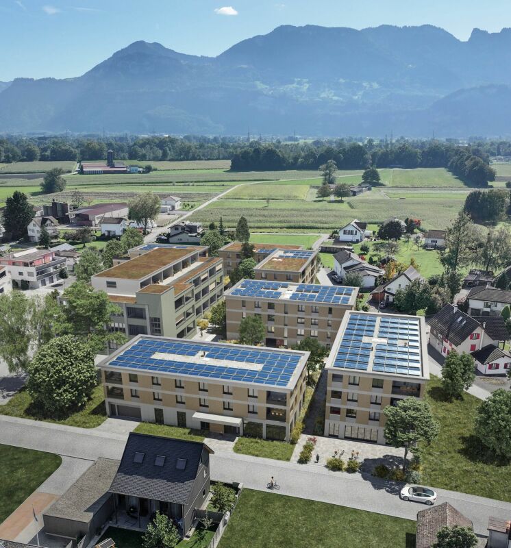 Luftaufnahme einer Wohnanlage mit Solardächern vor Bergkulisse