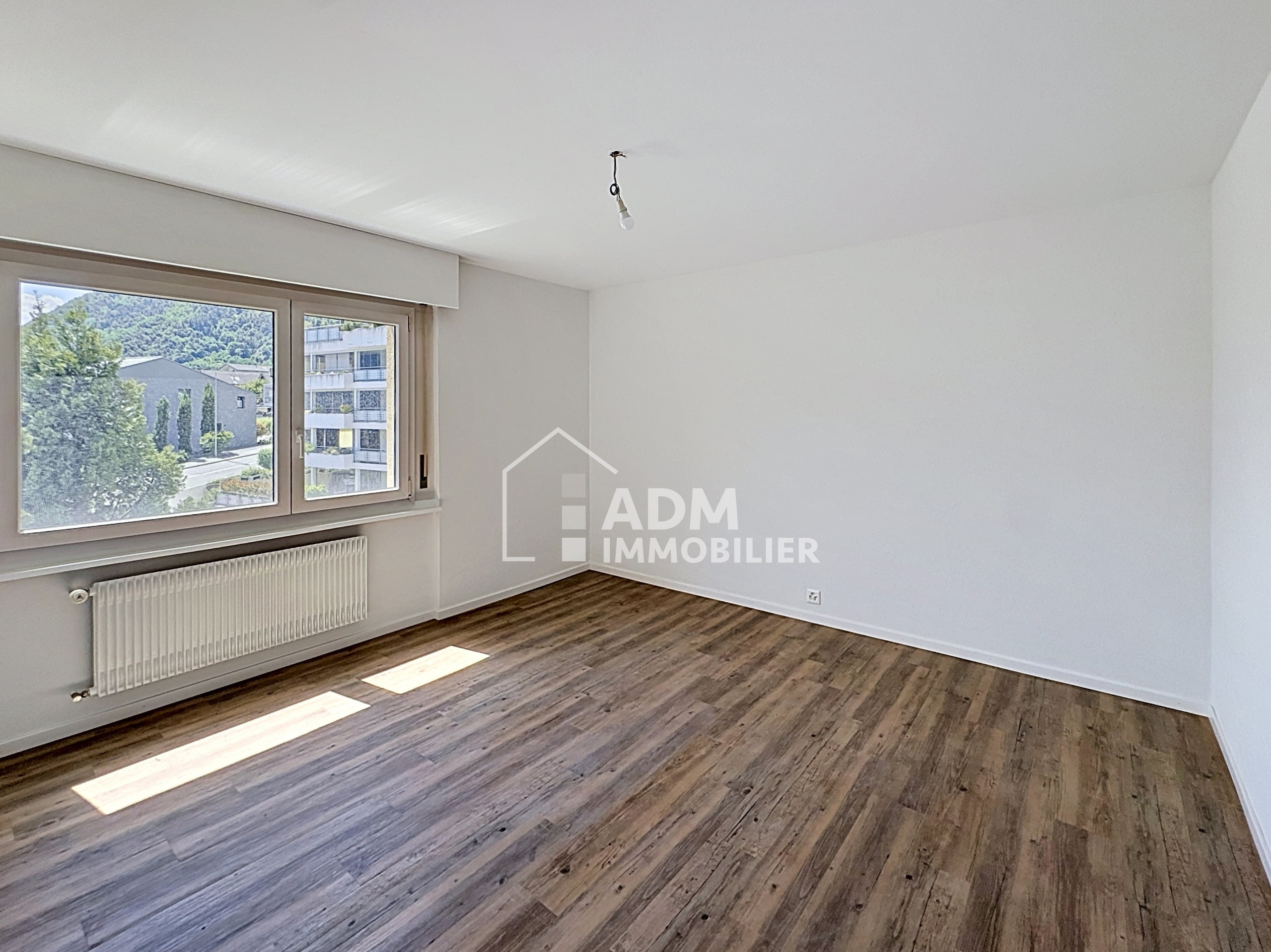 Leeres, helles Zimmer mit Fenster und Holzoptik-Boden