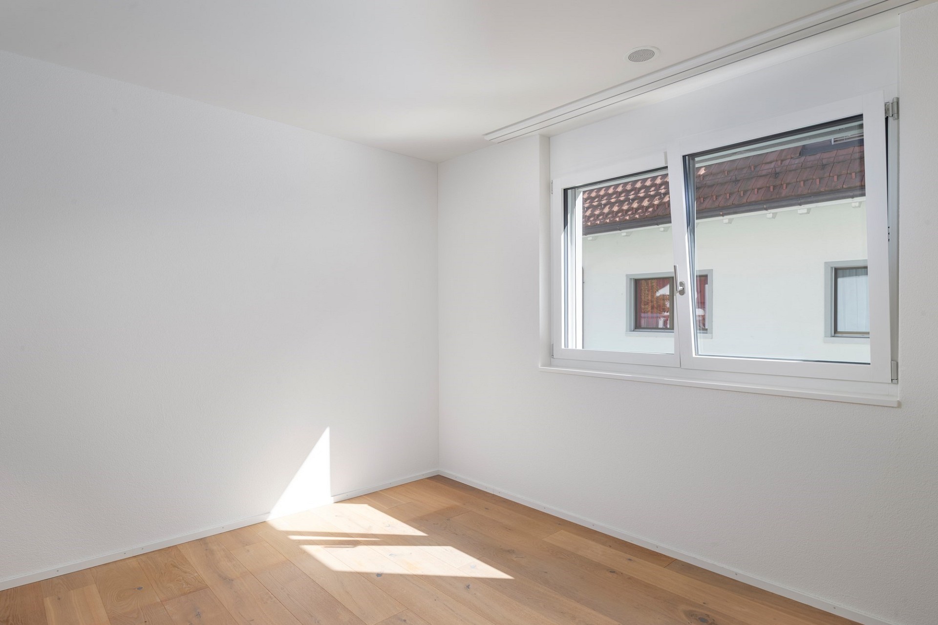 Helles, leeres Zimmer mit Fenster und Holzboden