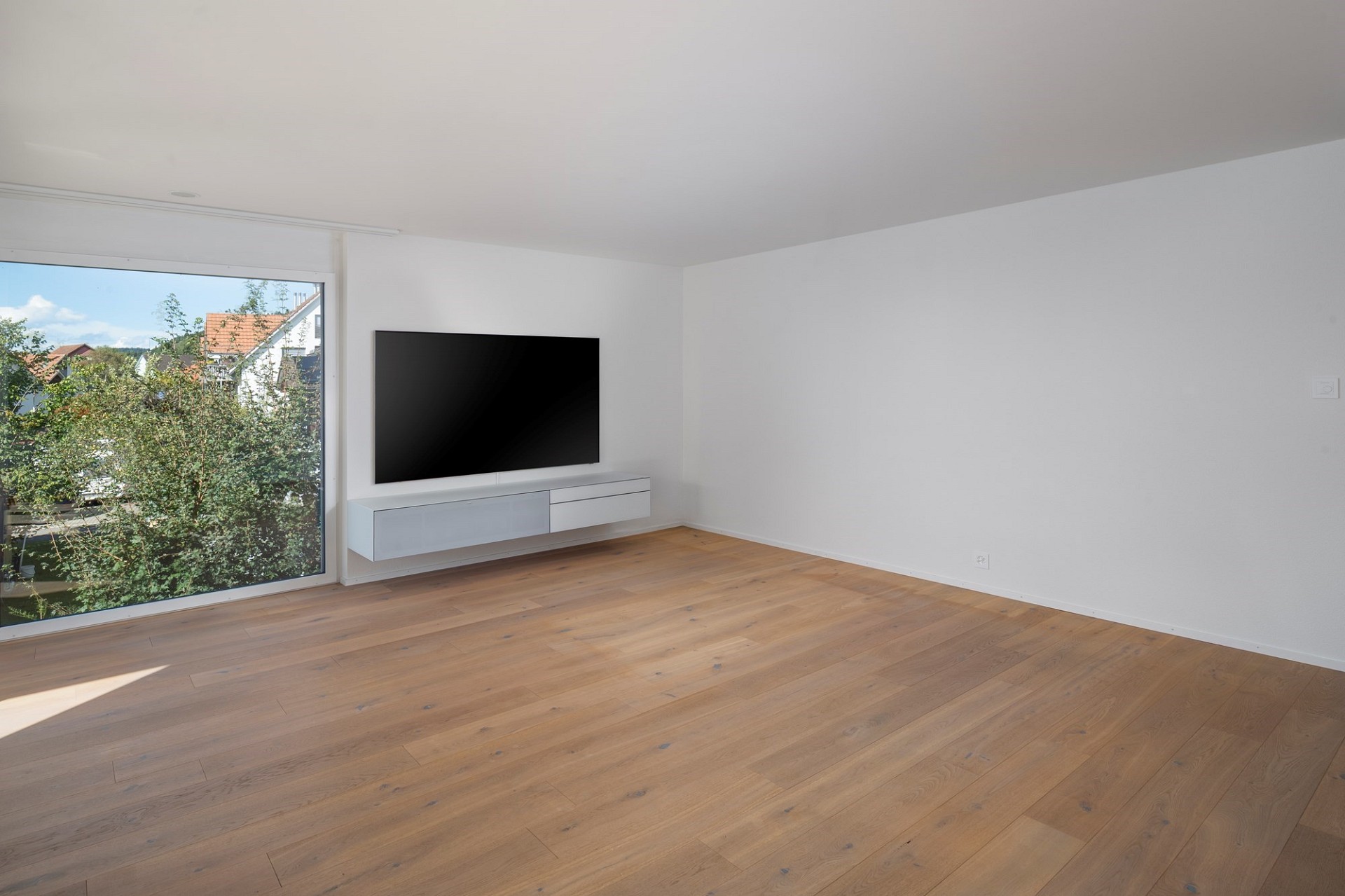 Helles, leeres Wohnzimmer mit großem Fenster und TV-Wand