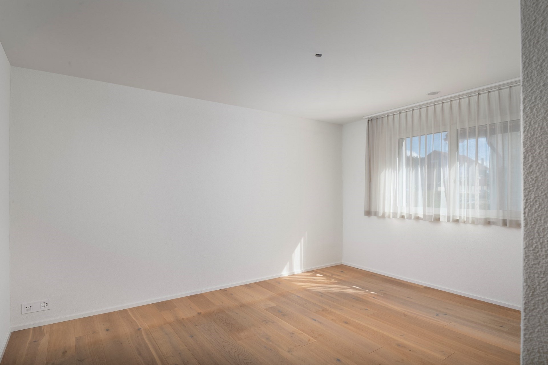 Helles, leeres Zimmer mit Parkett und Fenster