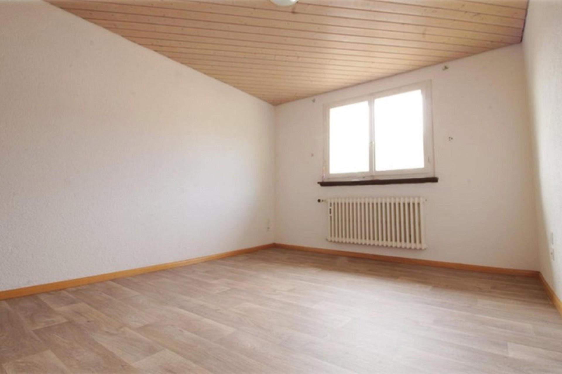 Leerer Dachgeschossraum mit Fenster und Heizkörper
