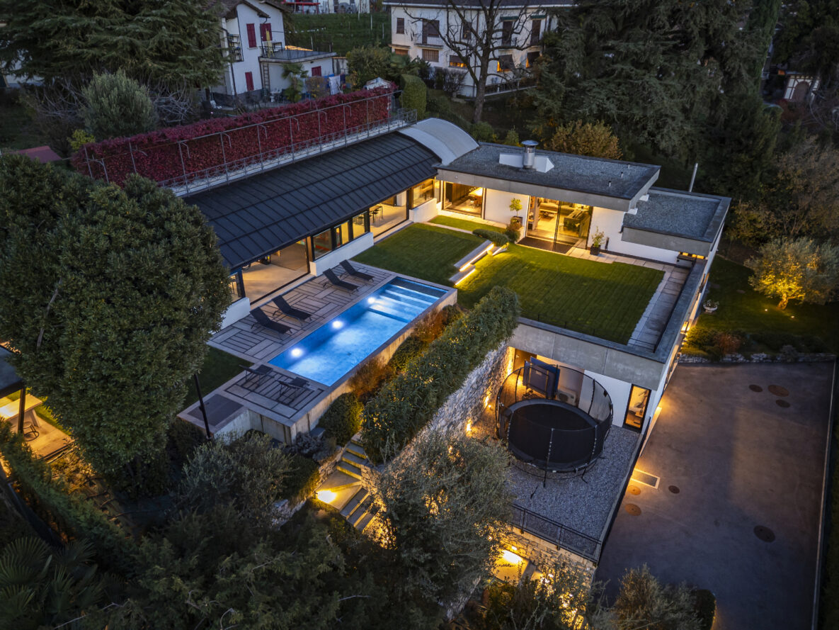 Drohnenaufnahme einer modernen Villa mit Pool und Dachgarten bei Abendlicht
