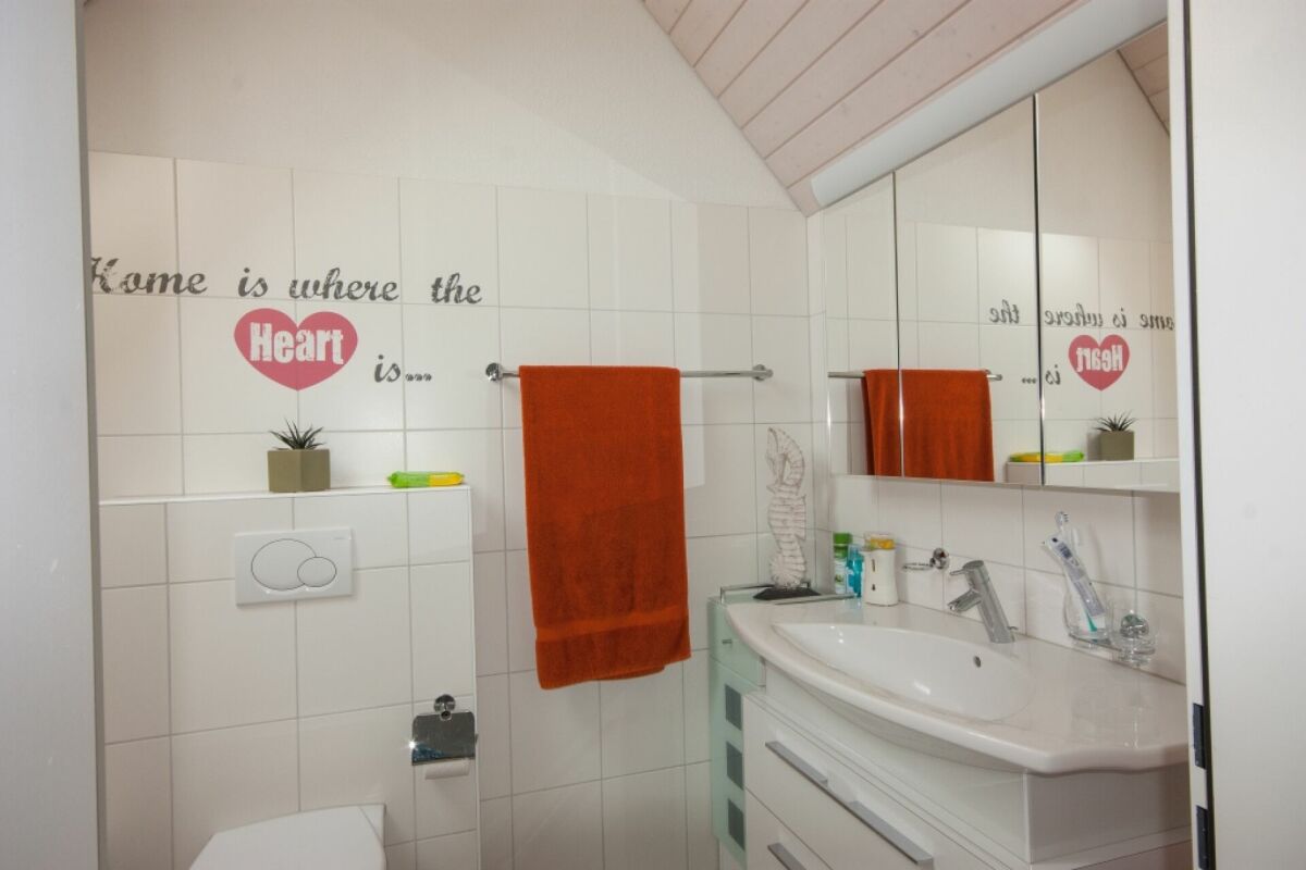 Helles, kleines Badezimmer mit orangefarbenem Handtuch und Spiegelschrank