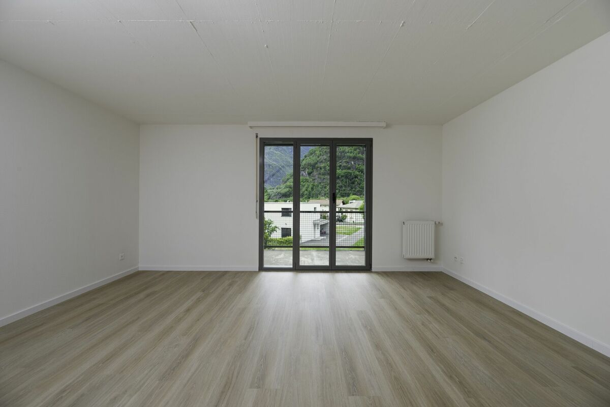 Leerer, heller Wohnraum mit Balkon- bzw. Terrassentür und Bergblick