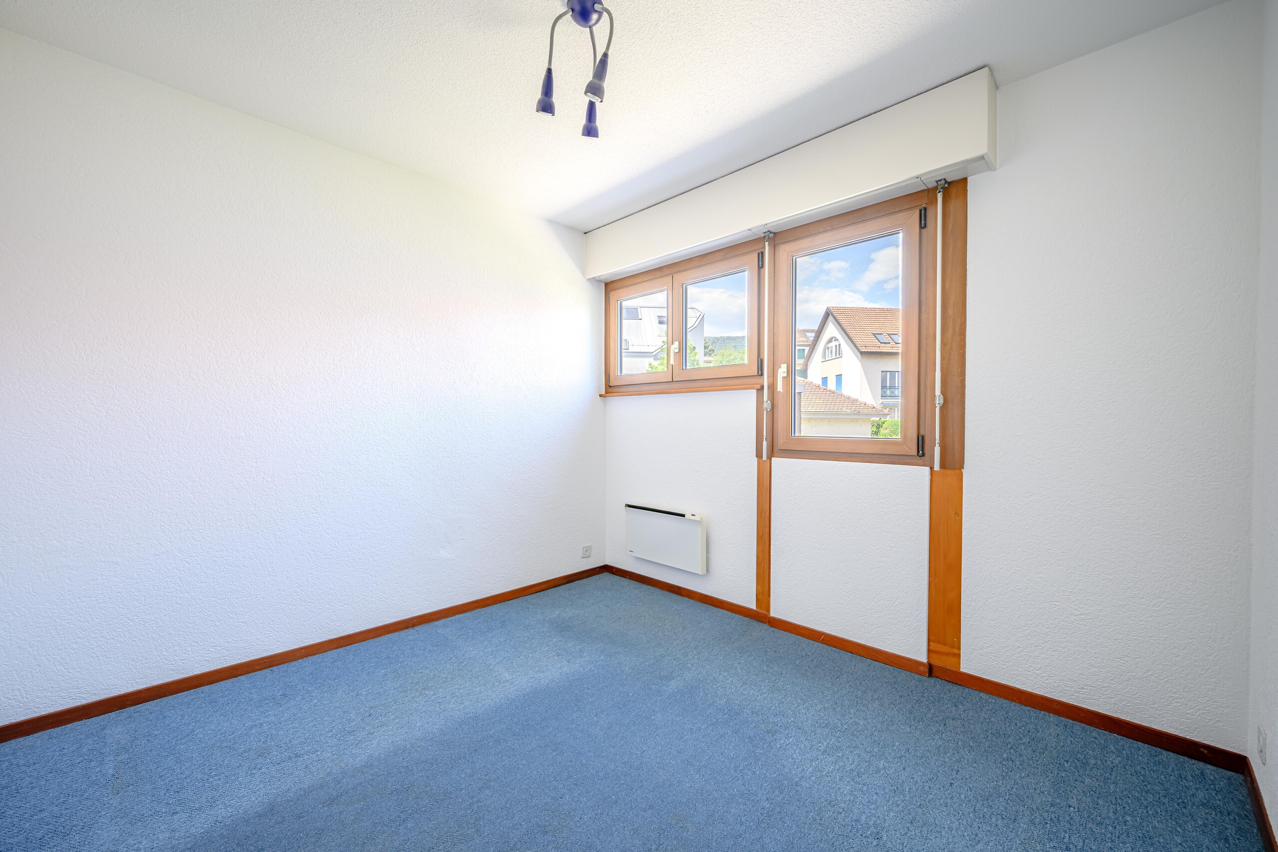Helles, leeres Zimmer mit blauem Teppichboden und Holzfenstern