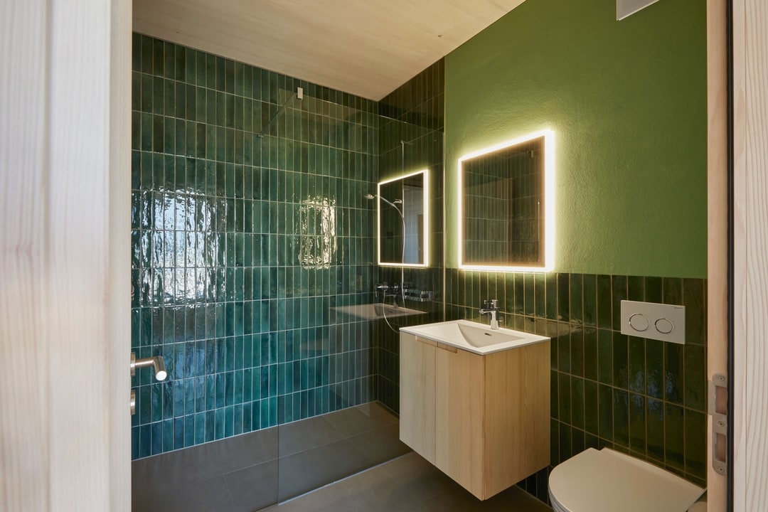 Modernes Badezimmer mit grünen Fliesen und beleuchteten Spiegeln
