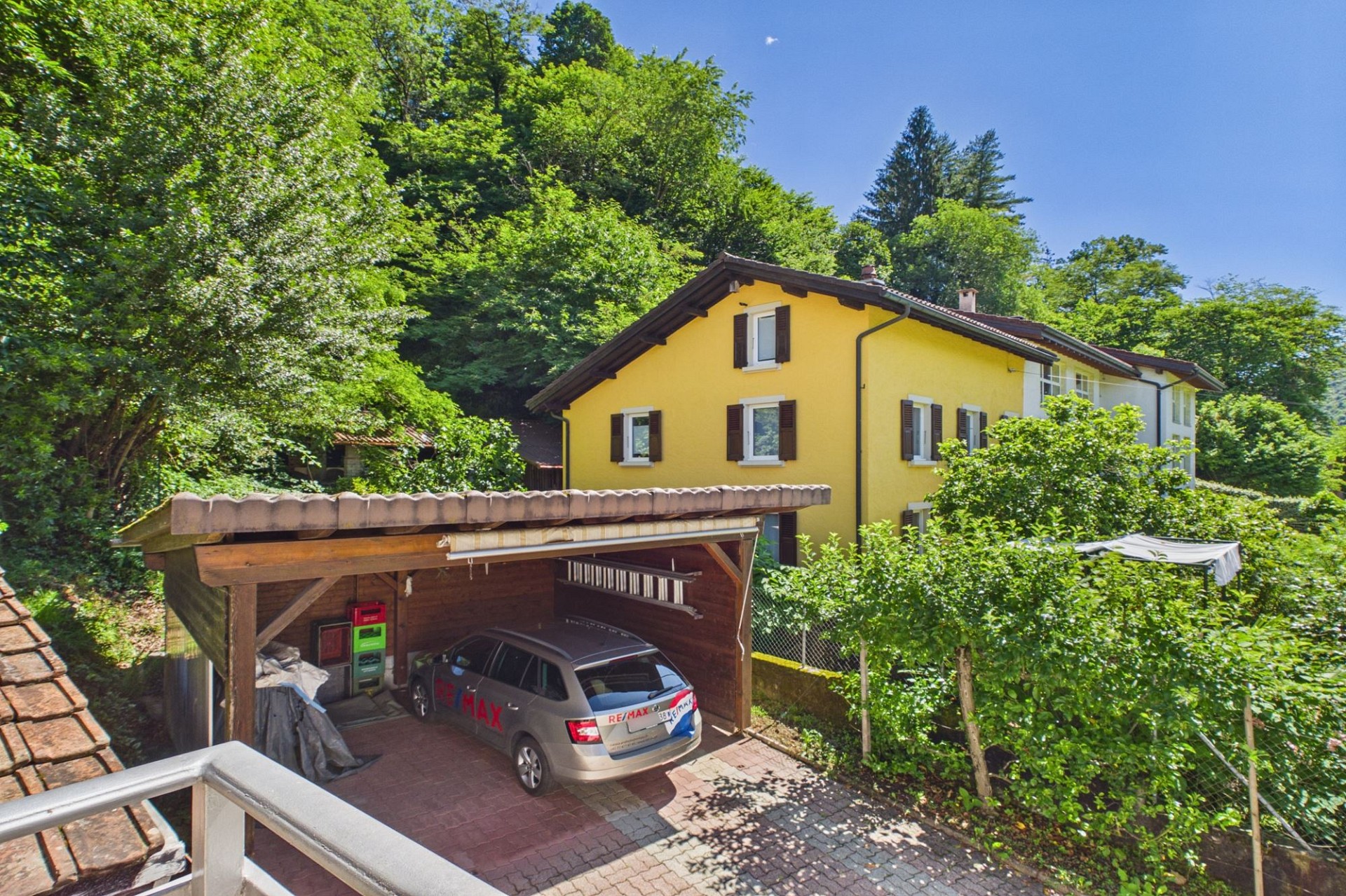 Gelbes Haus mit Carport in grüner Hanglage
