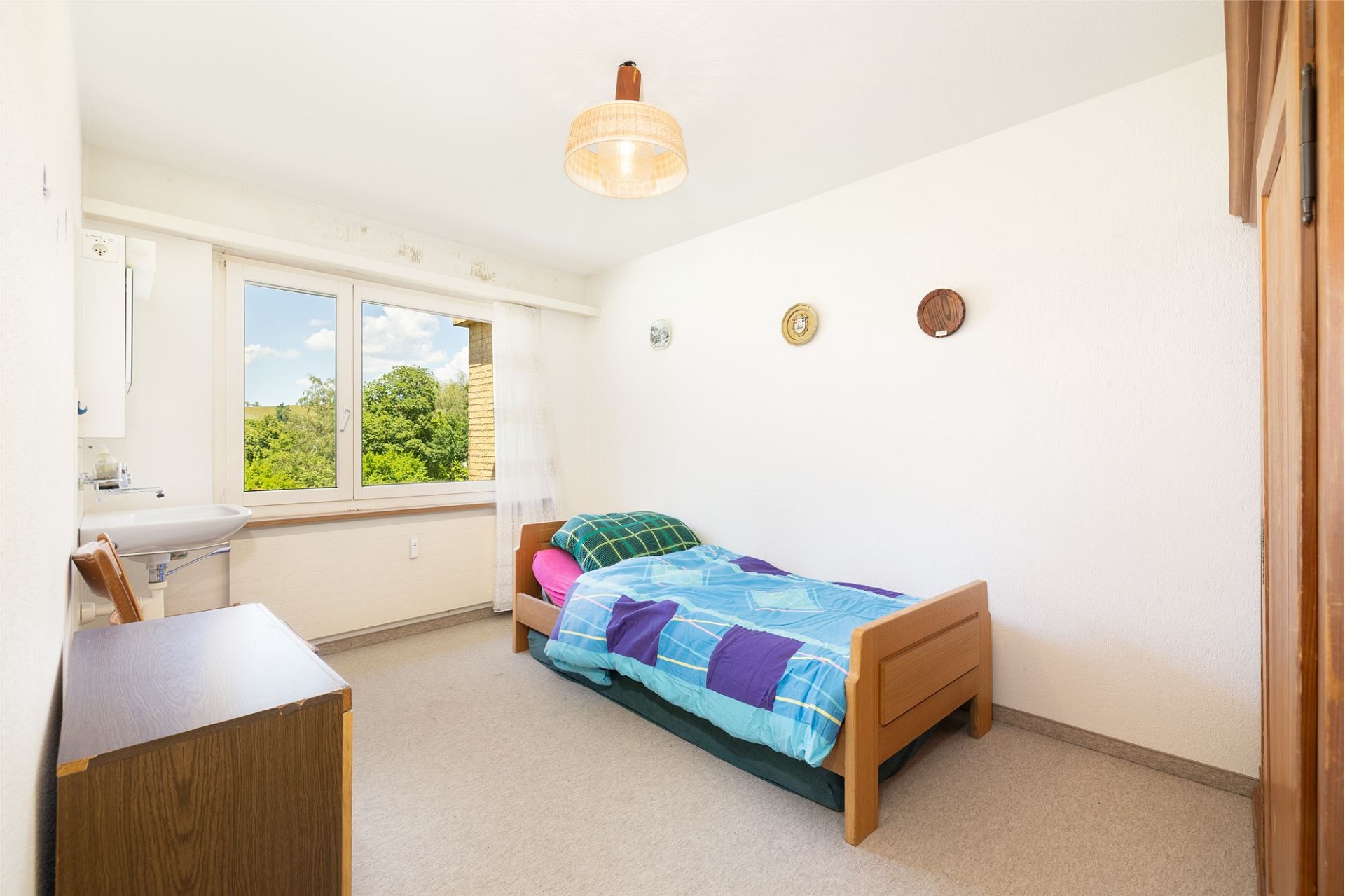 Ein kleines, helles Schlafzimmer mit Einzelbett und Fensterblick ins Grüne.