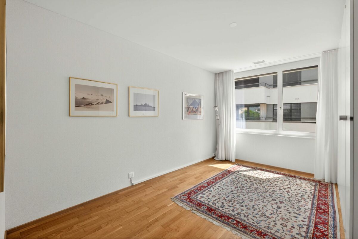 Helles, leer wirkendes Zimmer mit Holzfußboden und großem Fenster