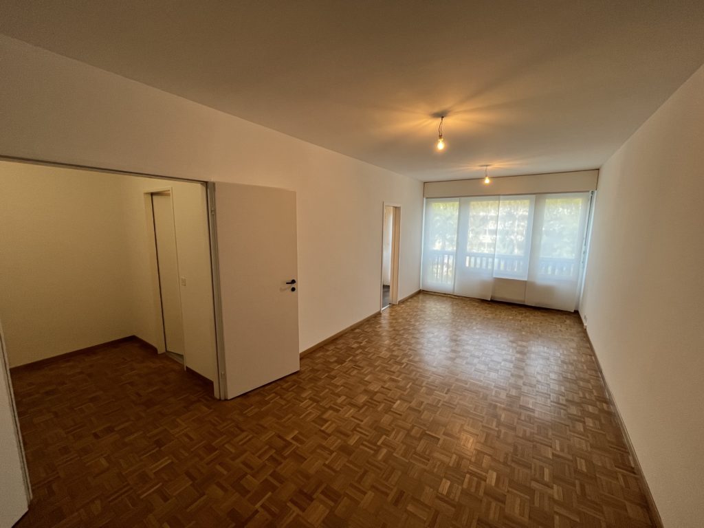 Leerer Wohnraum mit Parkett und Balkonfenstern