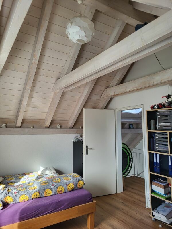 Dachzimmer mit Bett und offenem Dachstuhl