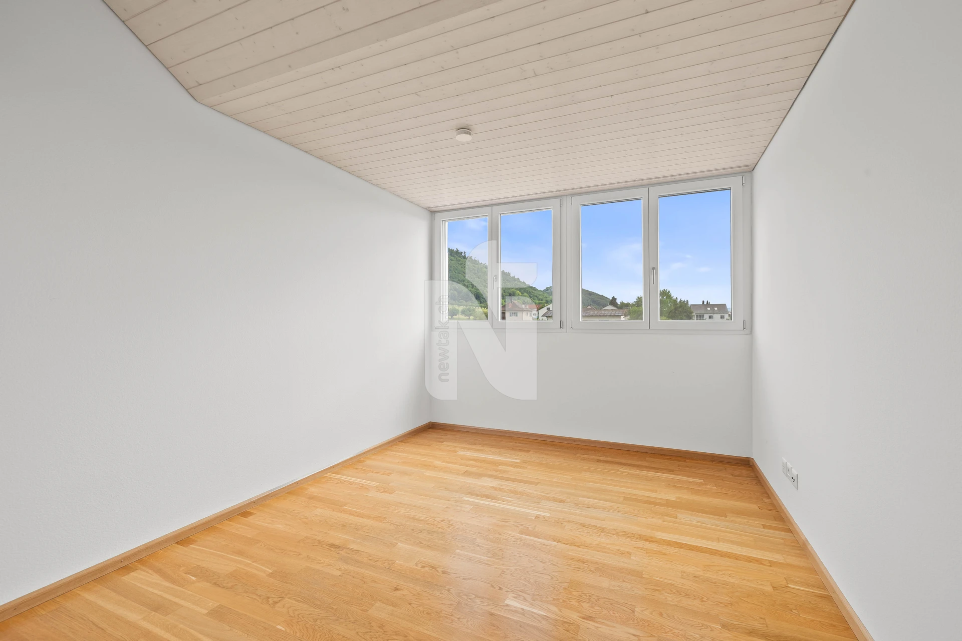 Helles, leeres Zimmer mit Holzdecke und großem Fenster