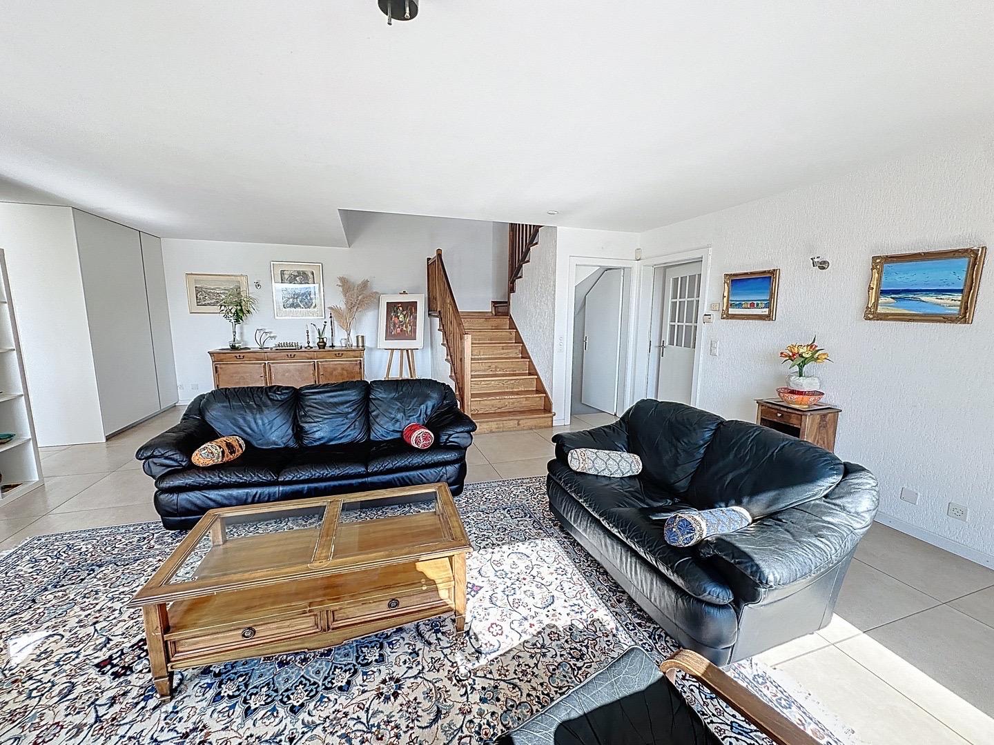 Helles Wohnzimmer mit Treppe und schwarzem Sofa