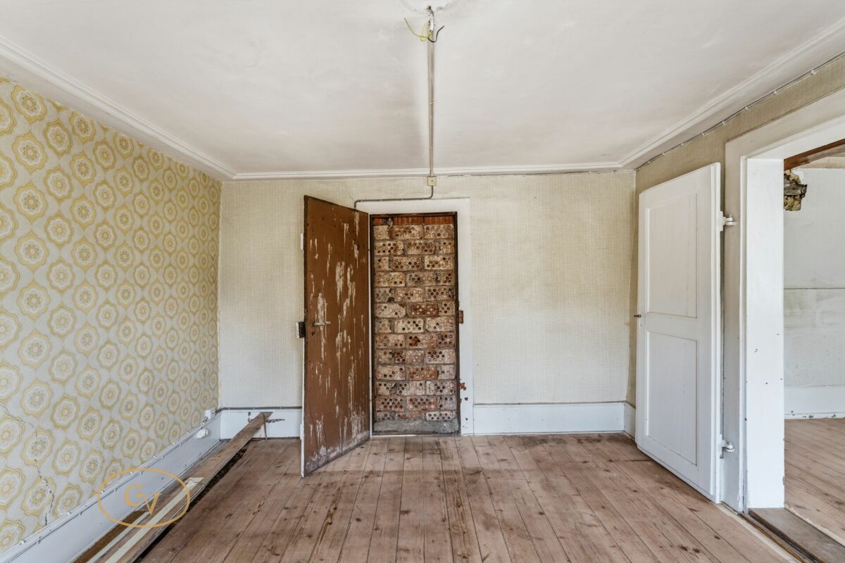 Renovierungsbedürftiges Zimmer mit abgenutztem Holzboden und alten Tapeten