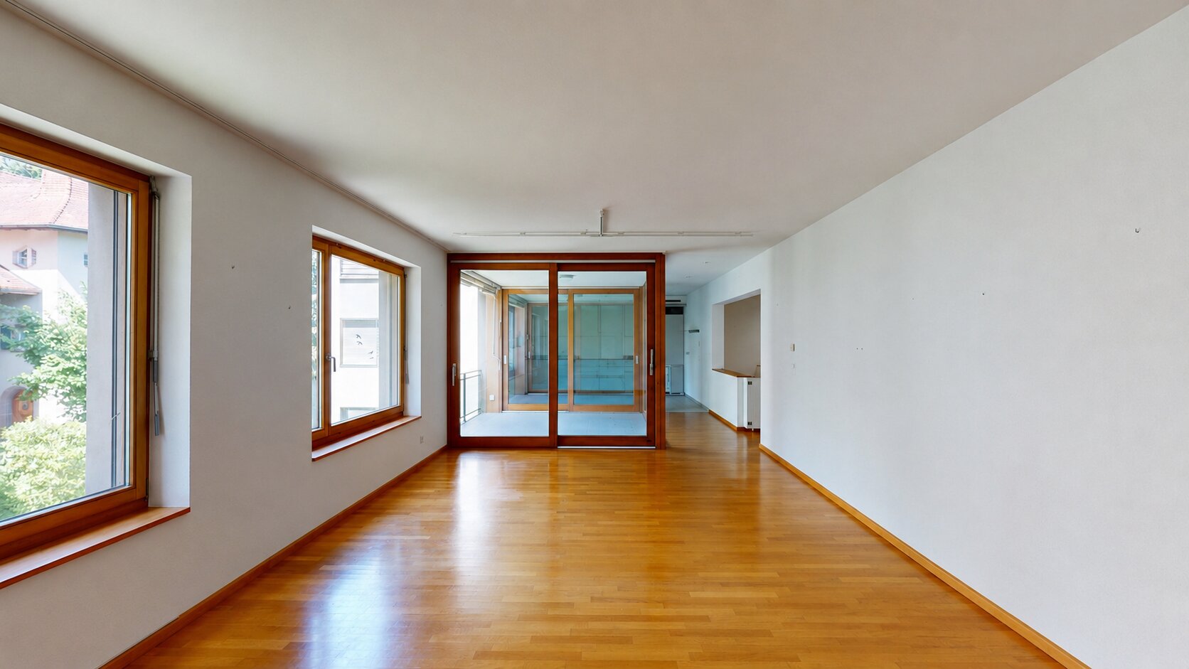 Heller, leerer Wohnraum mit Holzfußboden und großen Fenstern