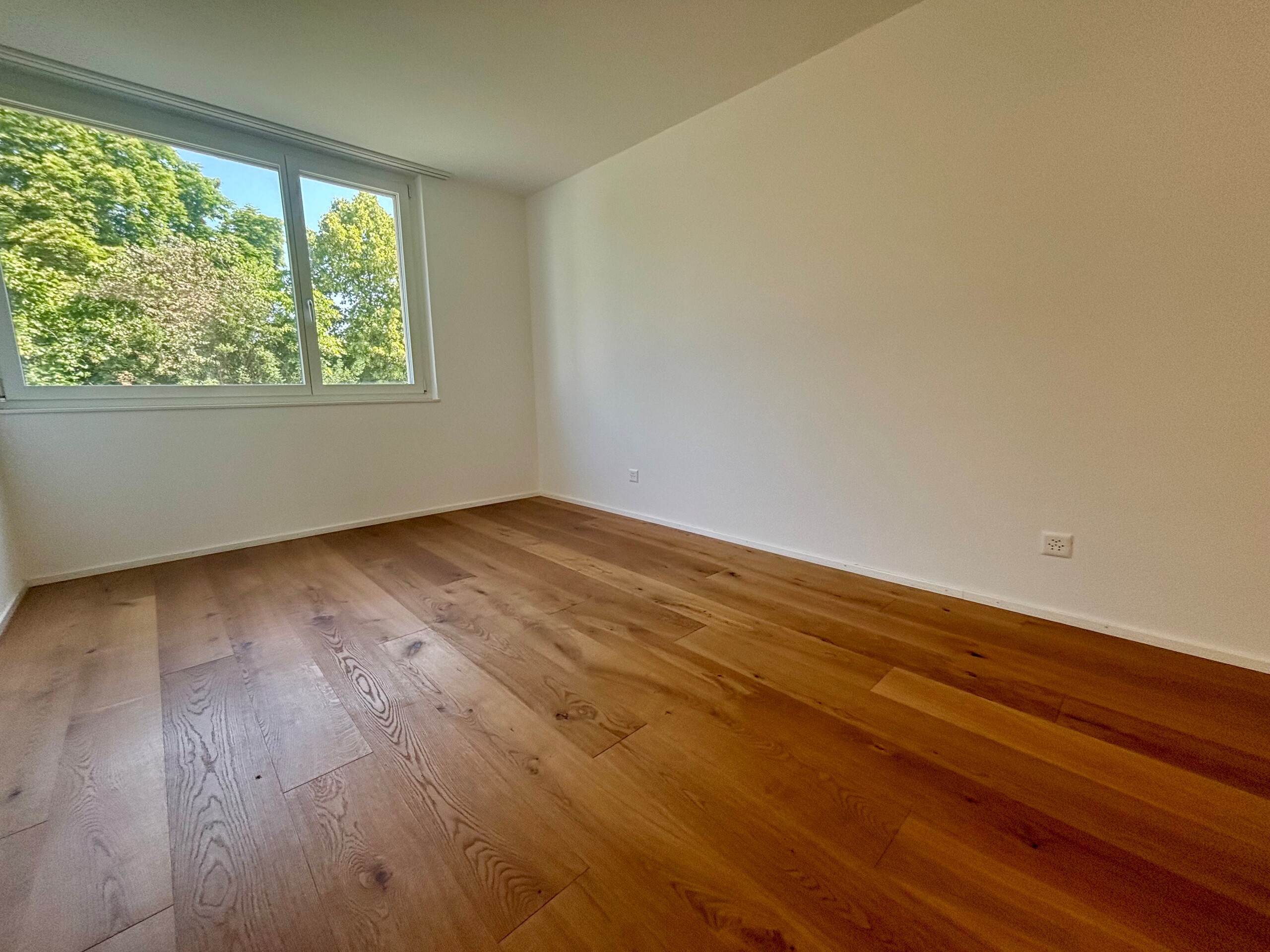 Leerer heller Raum mit Parkett und Fensterblick ins Grüne