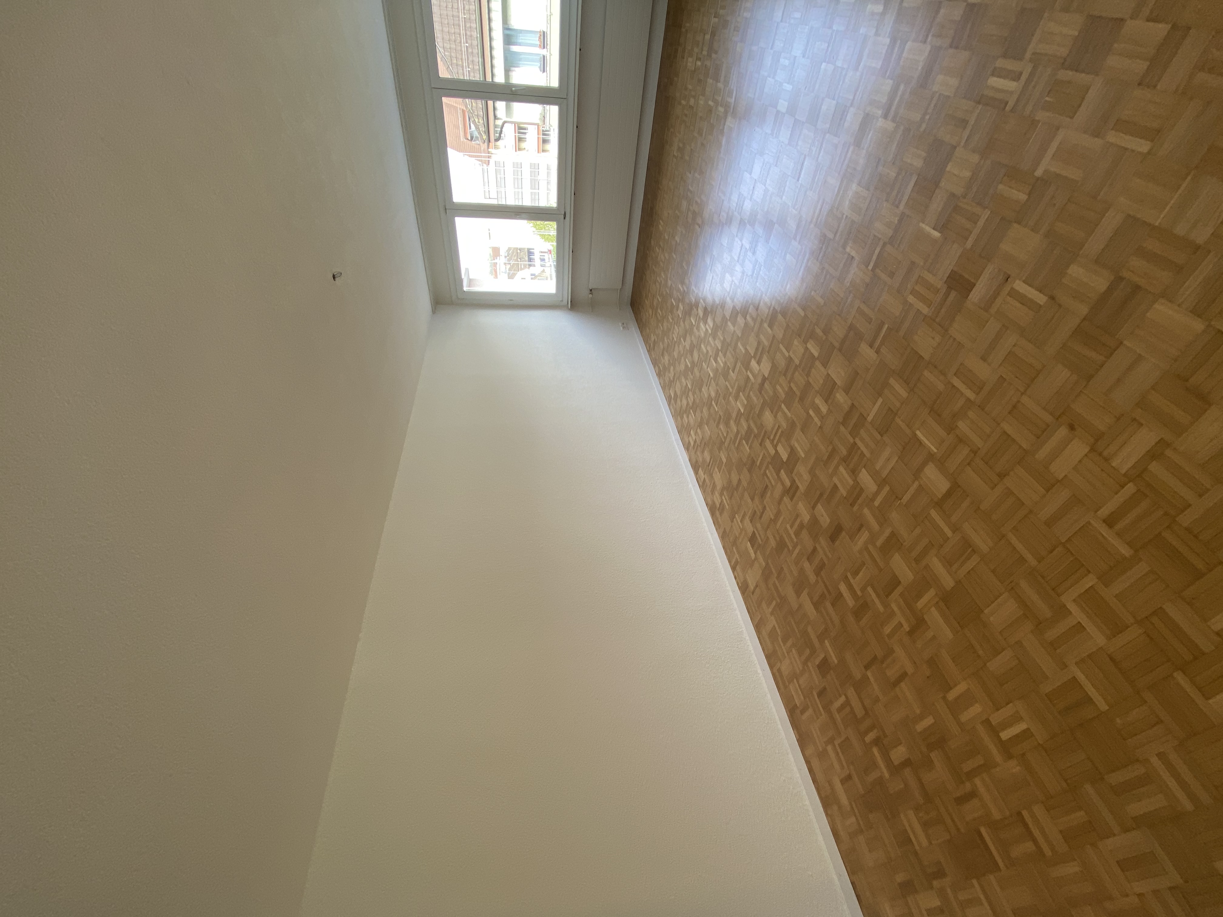 Leeres Wohnzimmer mit Parkett und großem Fenster