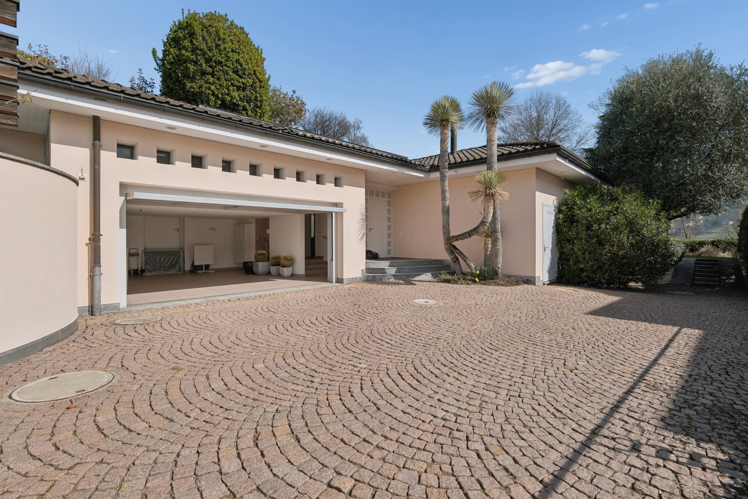 Mediterraner Hauseingang mit gepflastertem Vorplatz und offener Garage