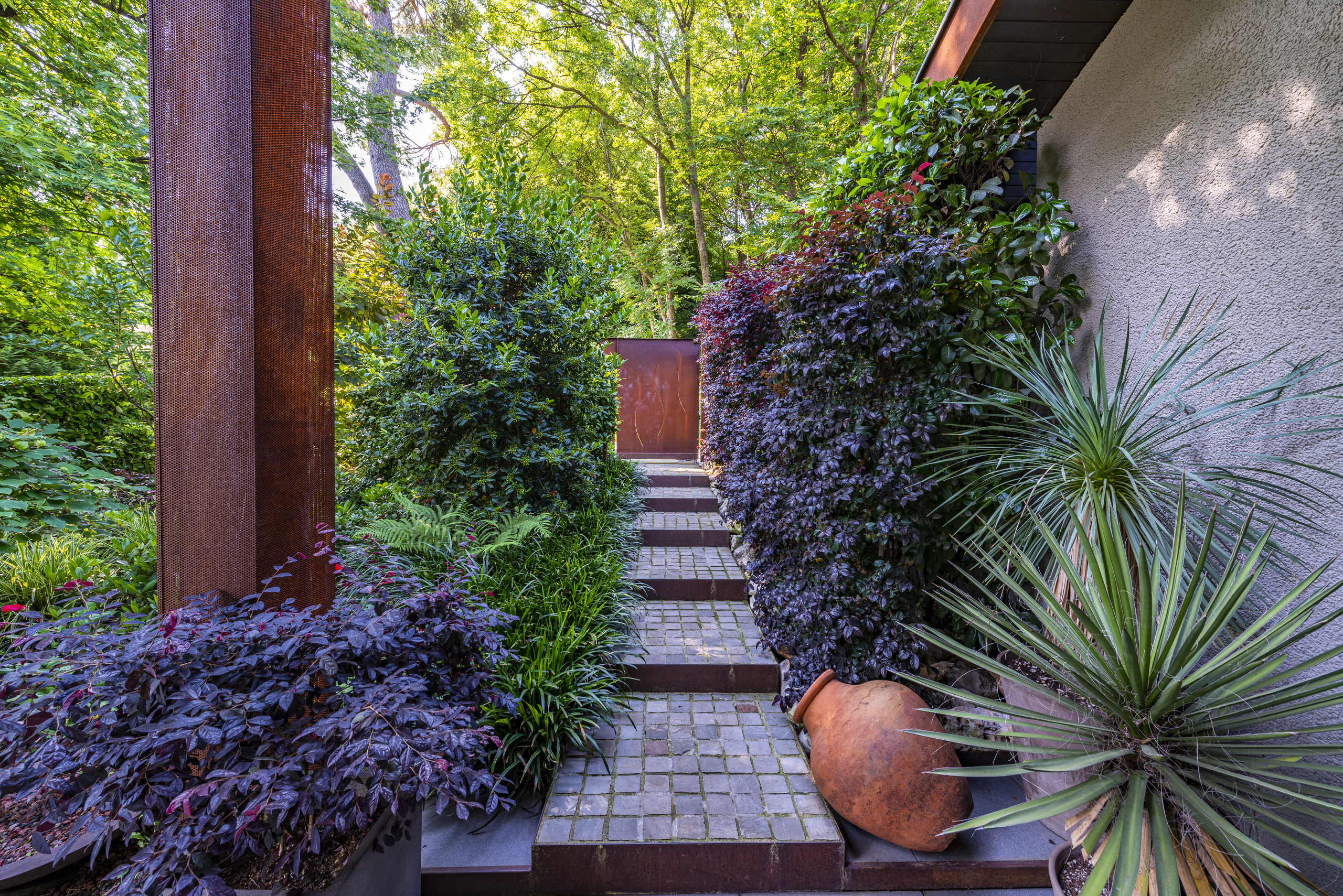 Gartenweg mit Metallskulptur und üppiger Bepflanzung