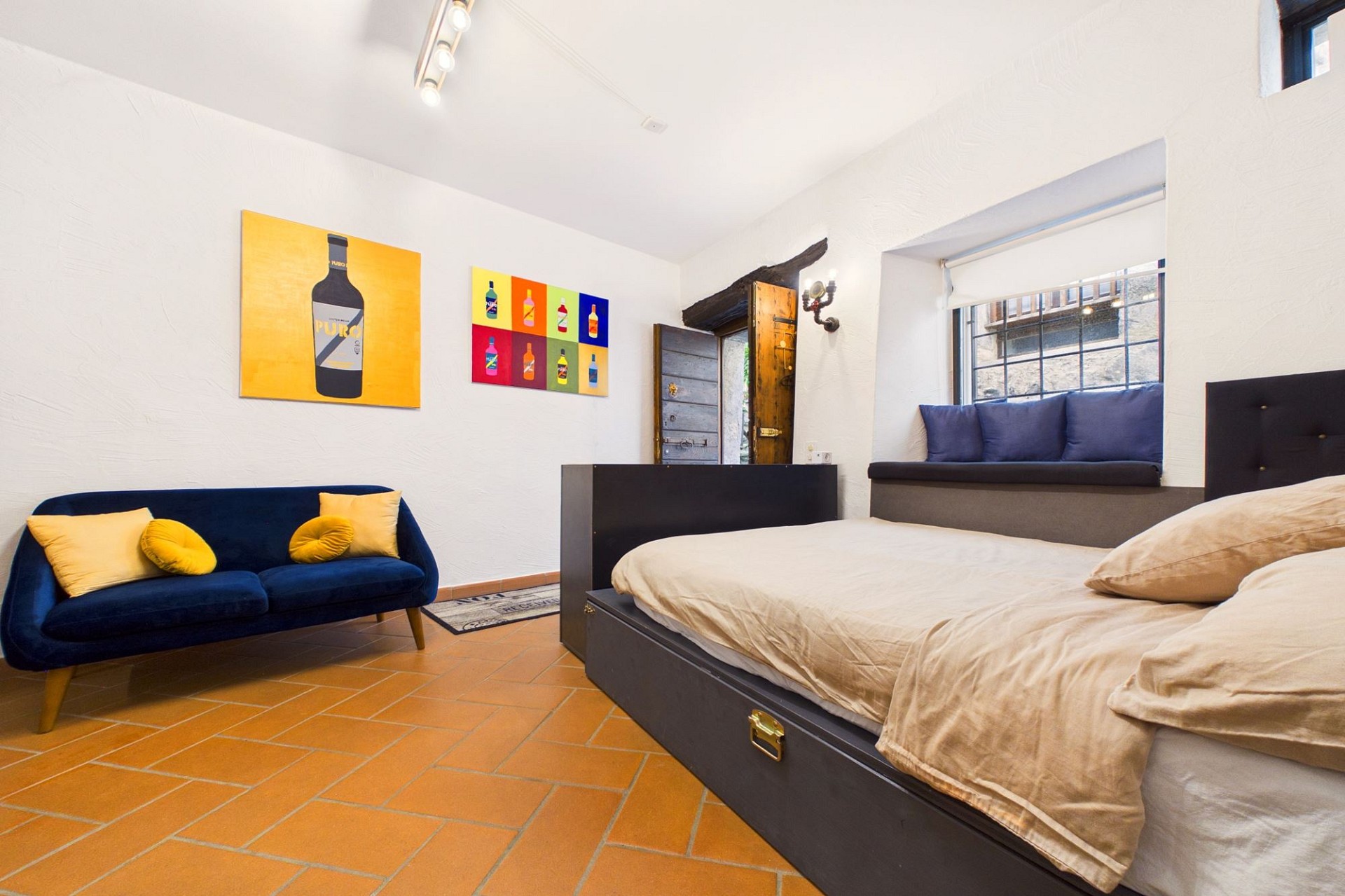 Schlafzimmer mit Terrakottaboden und bunten Kunstwerken