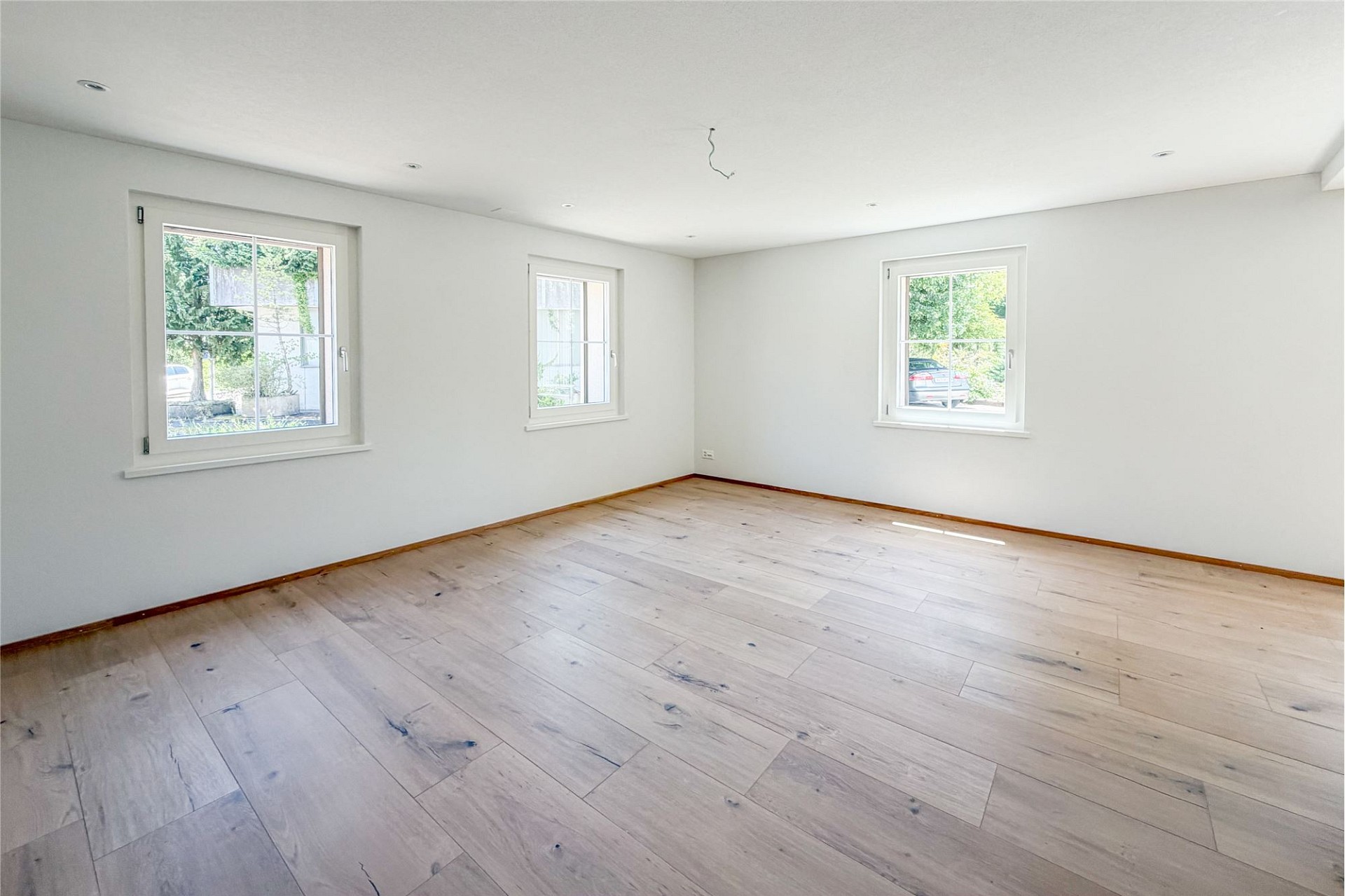 Heller leerer Raum mit drei Fenstern und Holzboden