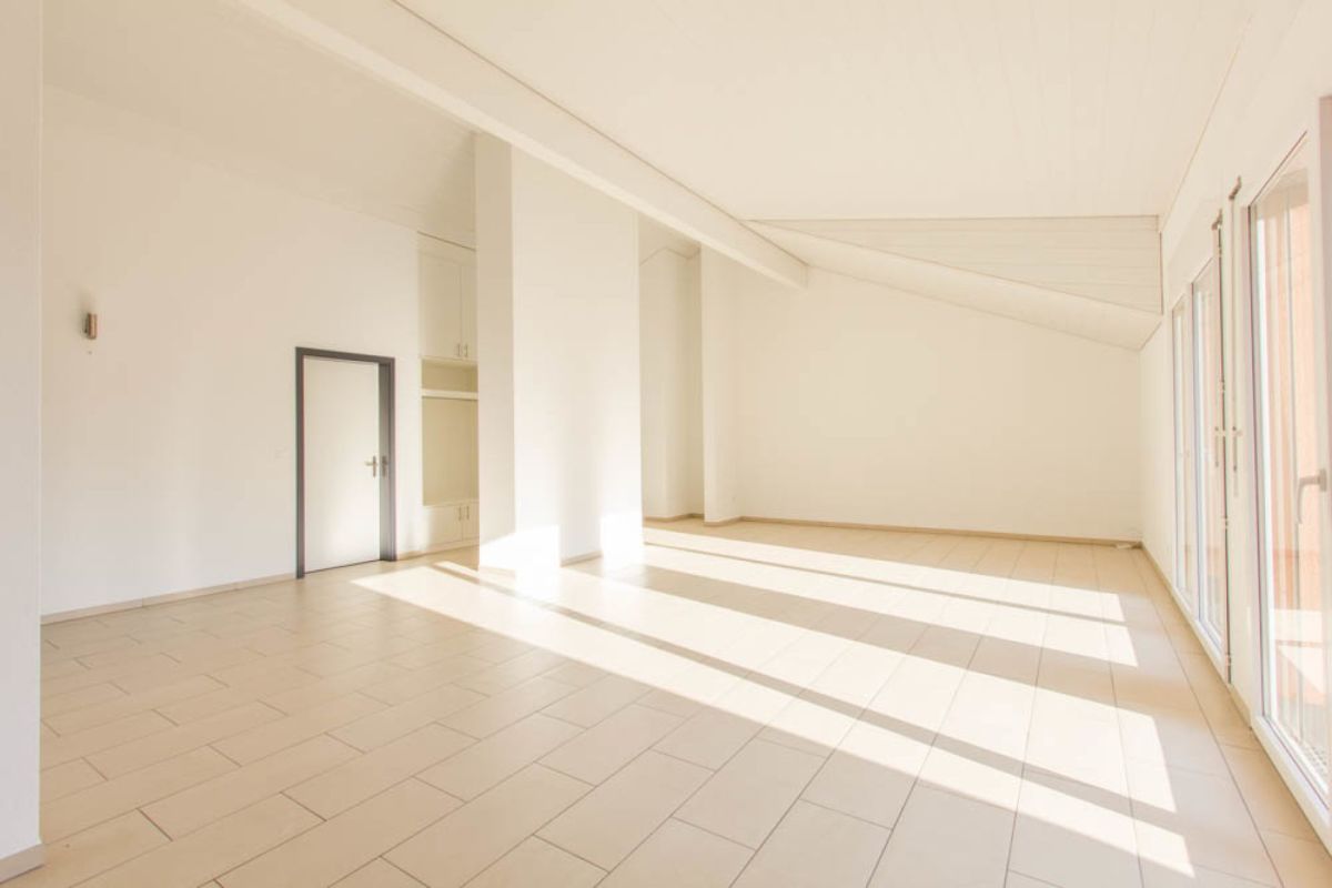 Heller leerer Wohnraum mit schräger Decke und großen Fenstern