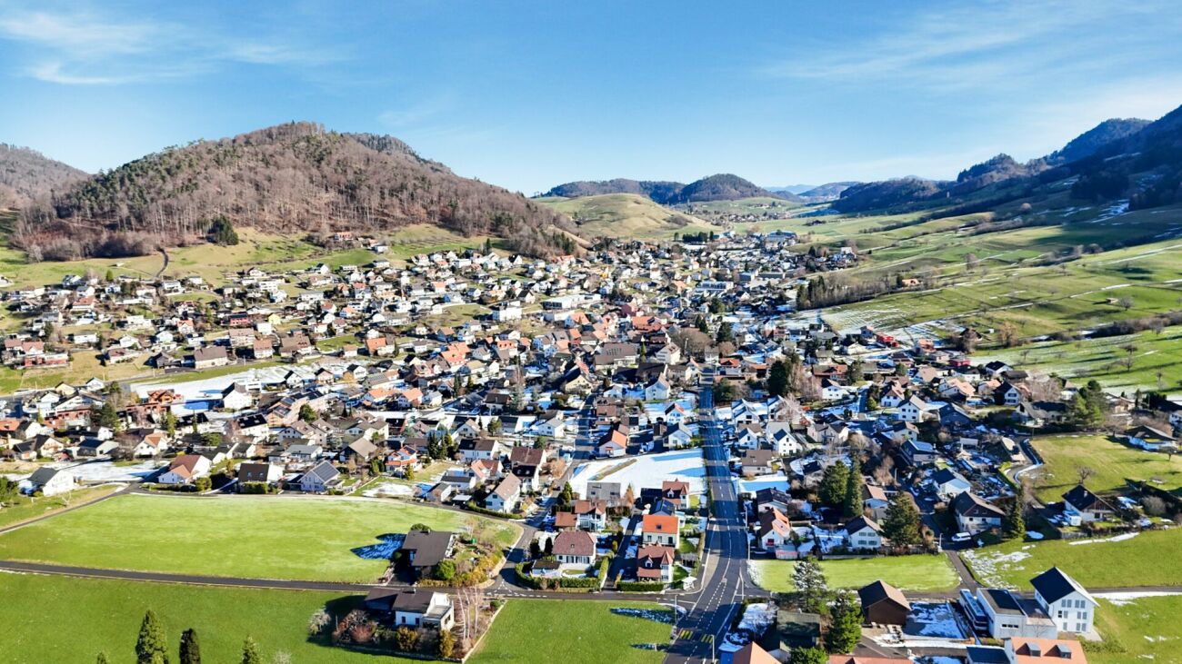 Luftaufnahme eines Ortes im Tal mit Wohnbebauung und Bergen