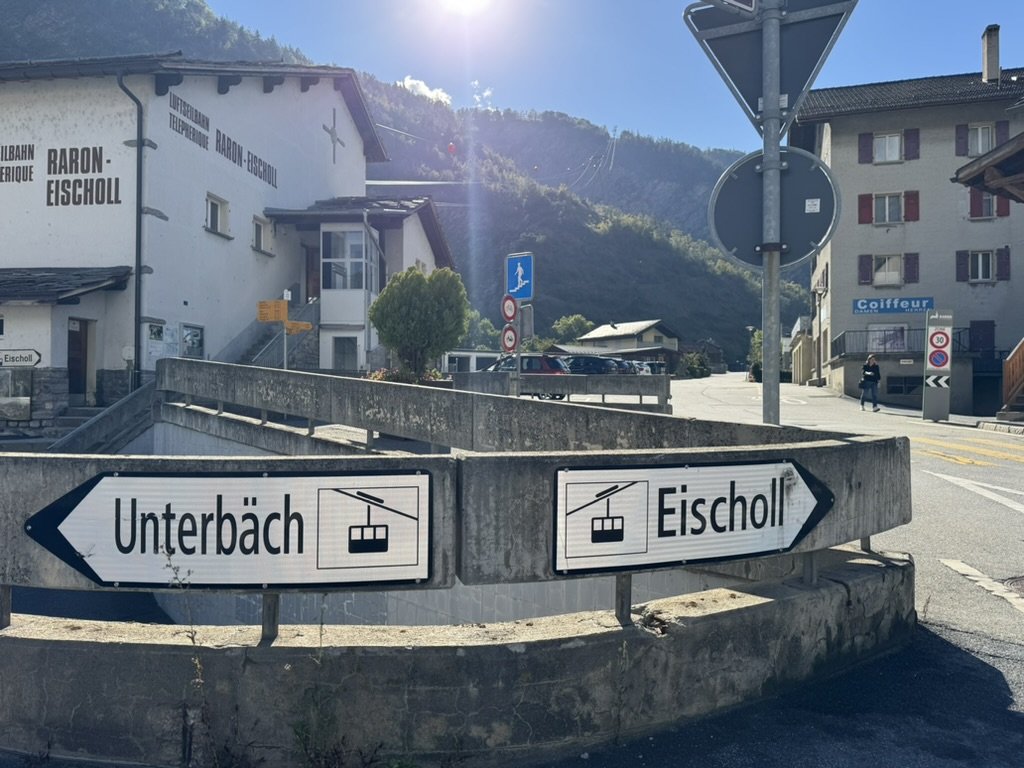 Straßenszene am Ortseingang mit Seilbahn-Hinweisschildern