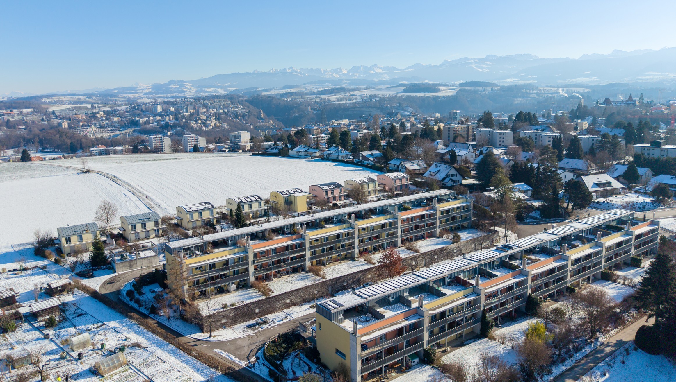 Luftaufnahme eines Wohngebiets im Schnee mit Bergpanorama