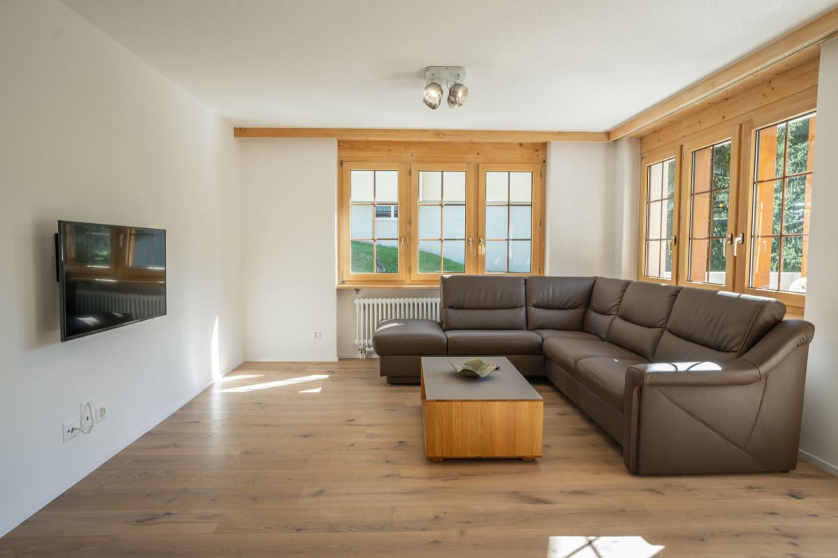 Wohnzimmer mit L-förmiger Ledergarnitur und Holzfenstern