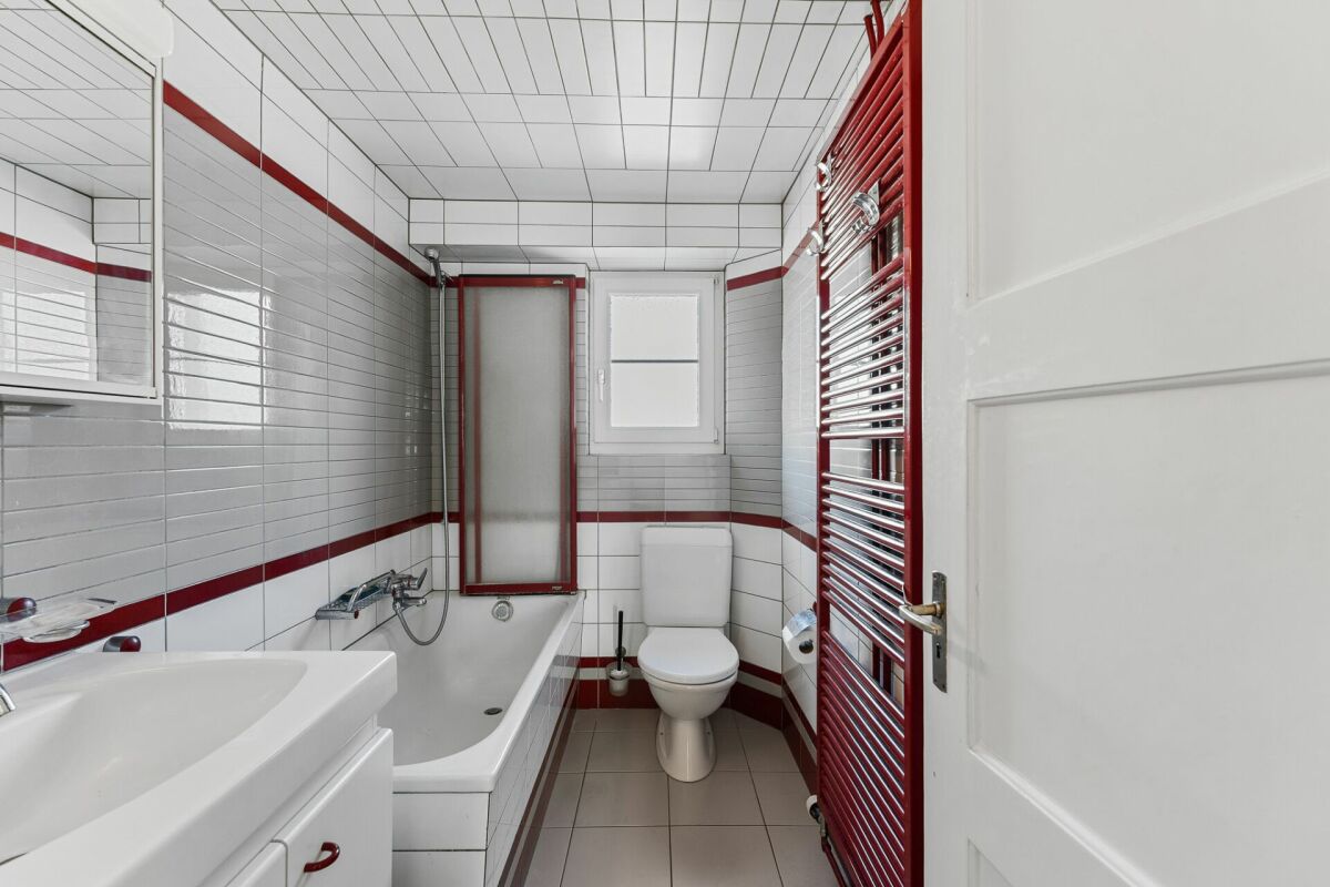 Kleines Badezimmer mit Badewanne und rotem Handtuchheizkörper