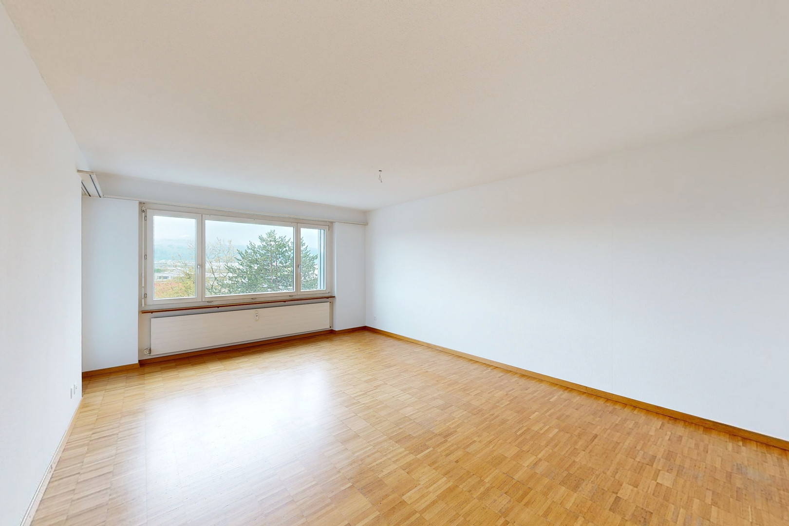 Helles, leeres Zimmer mit Parkett und großem Fenster
