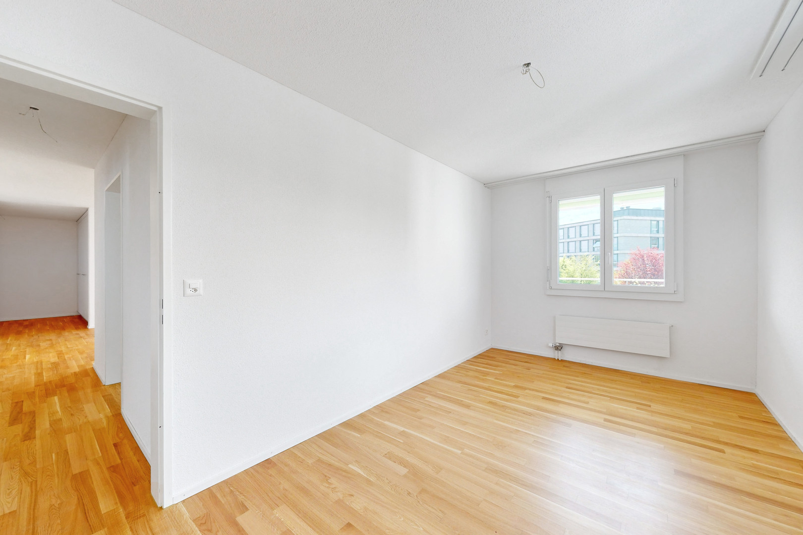 Helles, leeres Zimmer mit Parkett und Fenster