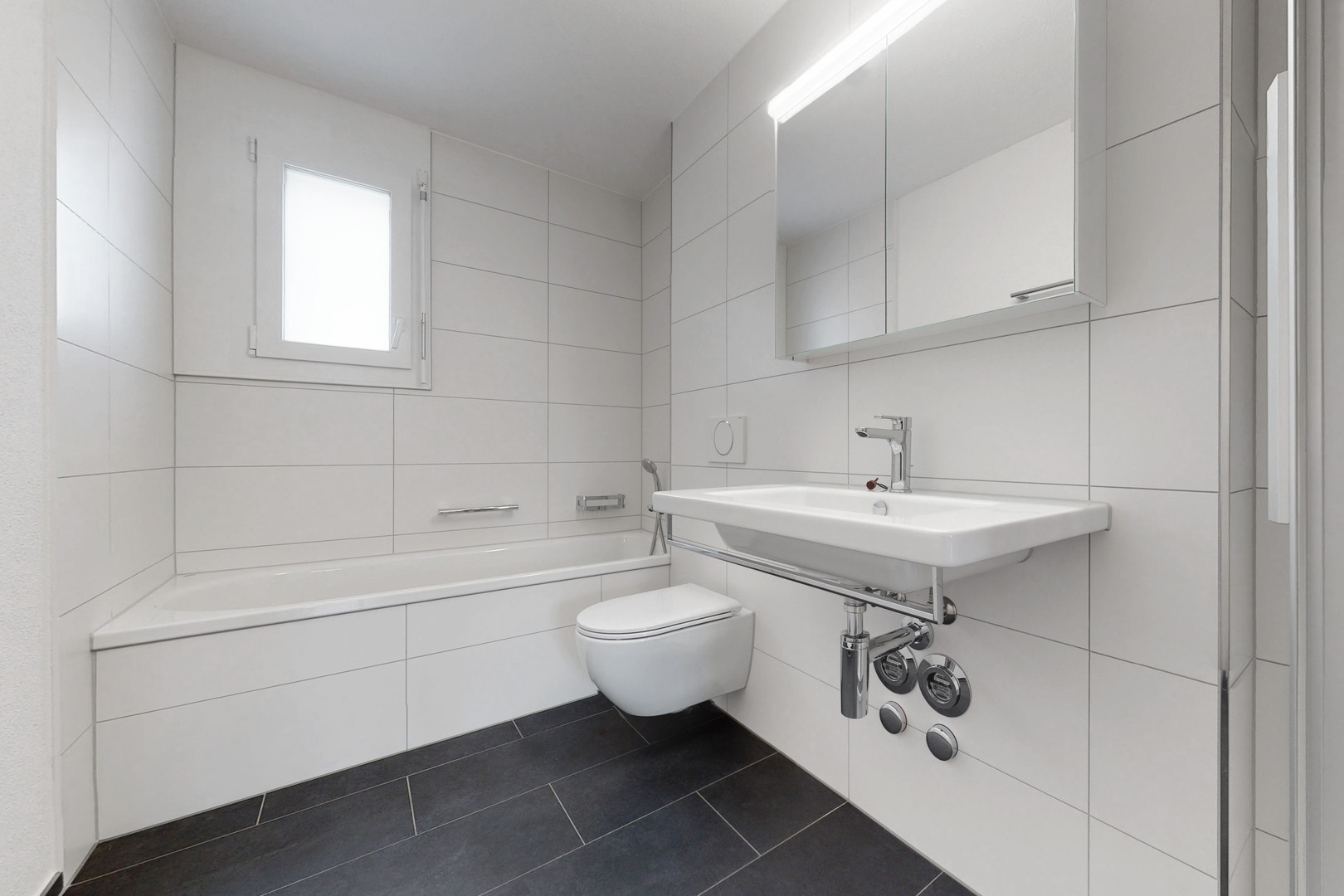 Modernes, weiß gefliestes Badezimmer mit Badewanne, wandhängendem WC und Waschtisch