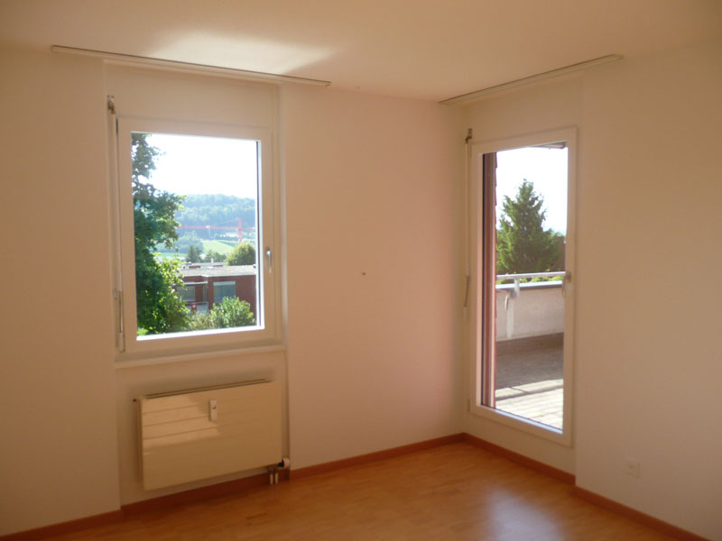 Helles, leeres Zimmer mit zwei Fenstern und Balkonzugang