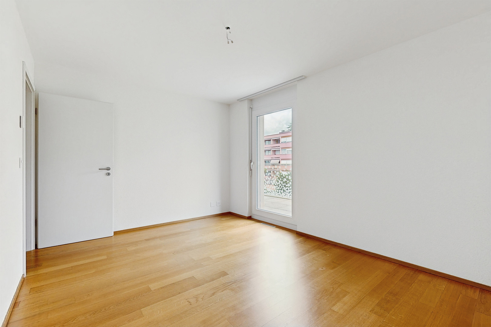 Heller leerer Raum mit Parkettboden und Balkonfenster