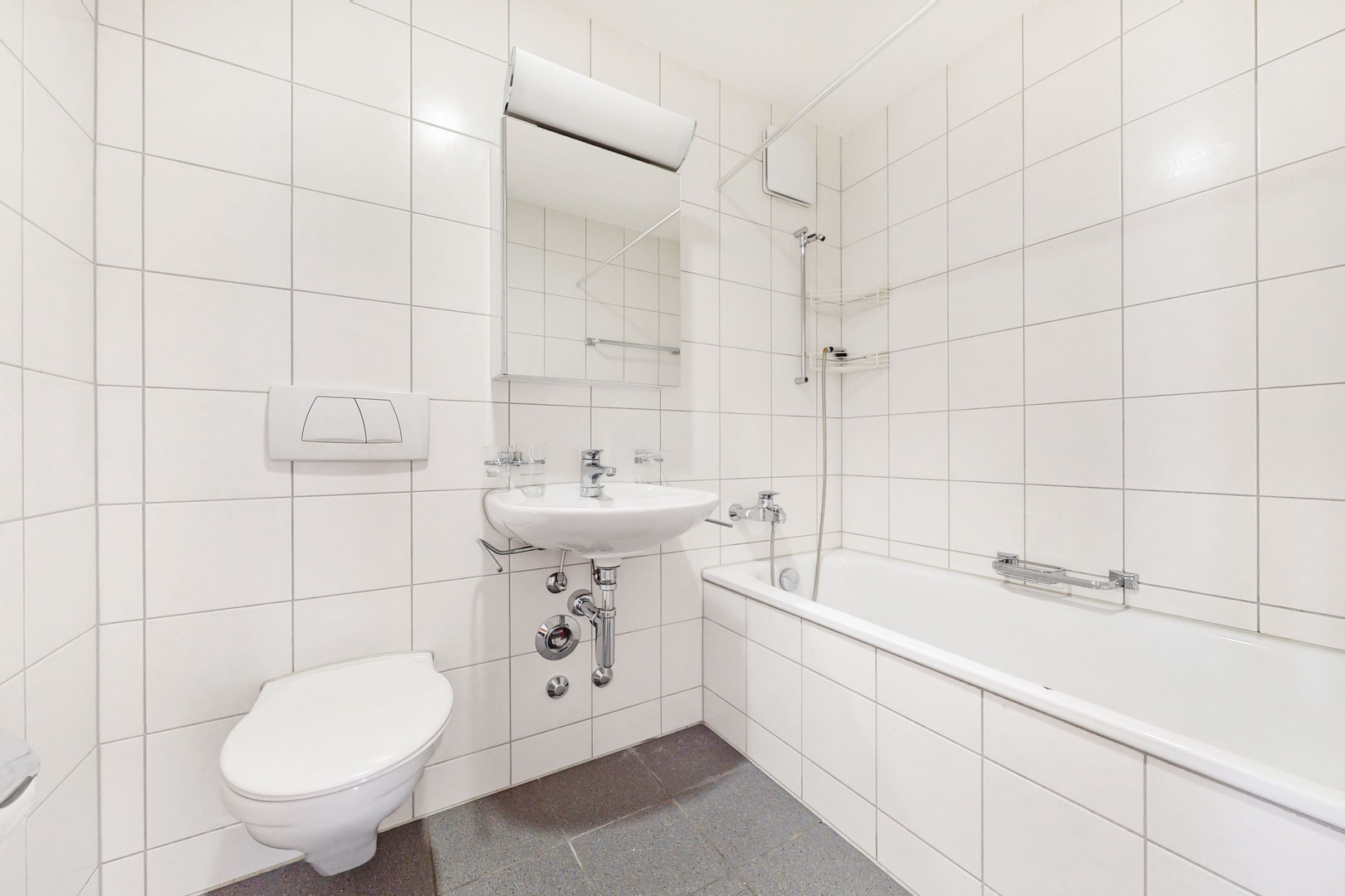 Kleines weiß gefliestes Badezimmer mit Wanne, Waschtisch und WC