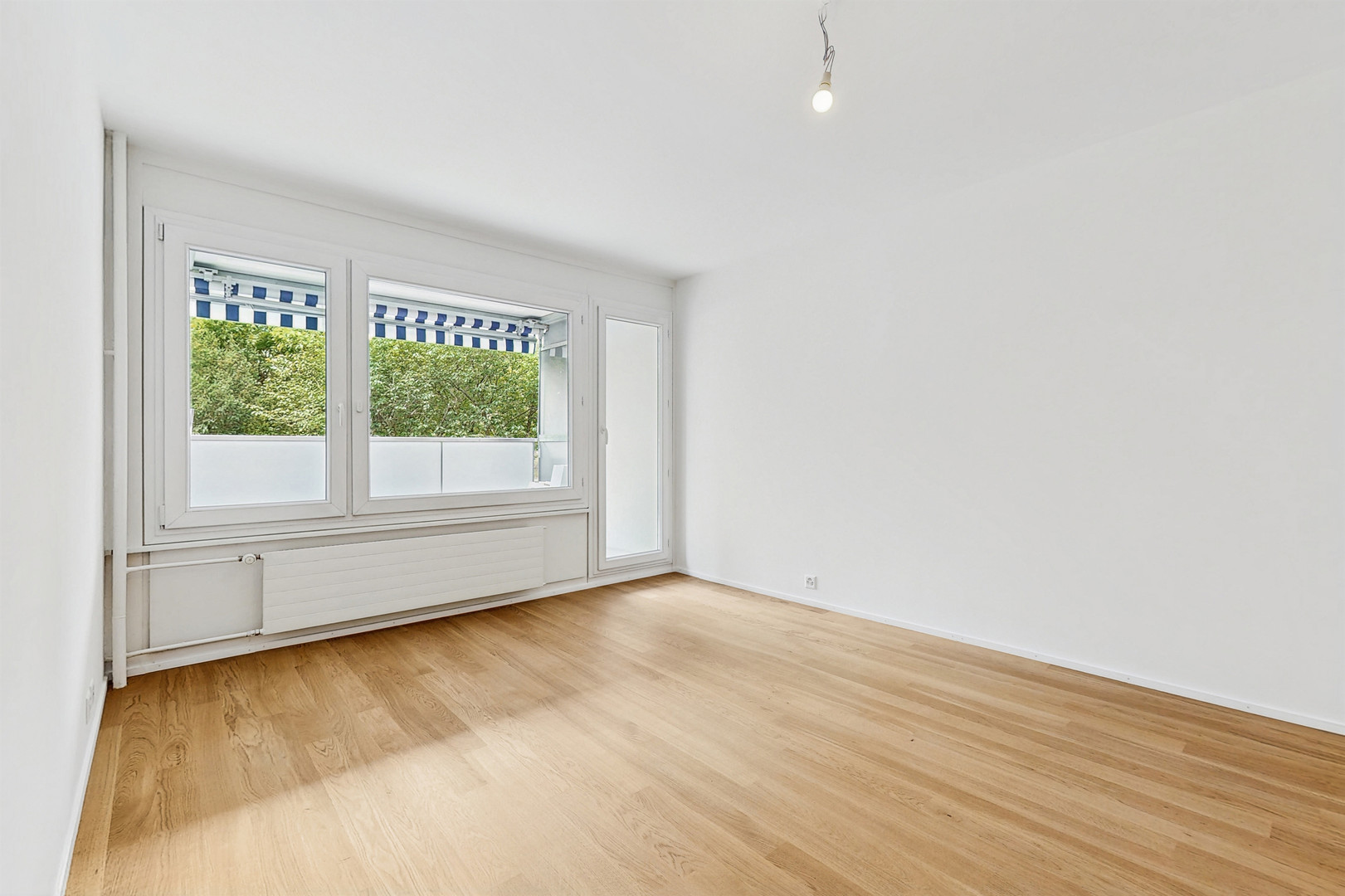Heller leerer Wohnraum mit Parkett und großem Fenster