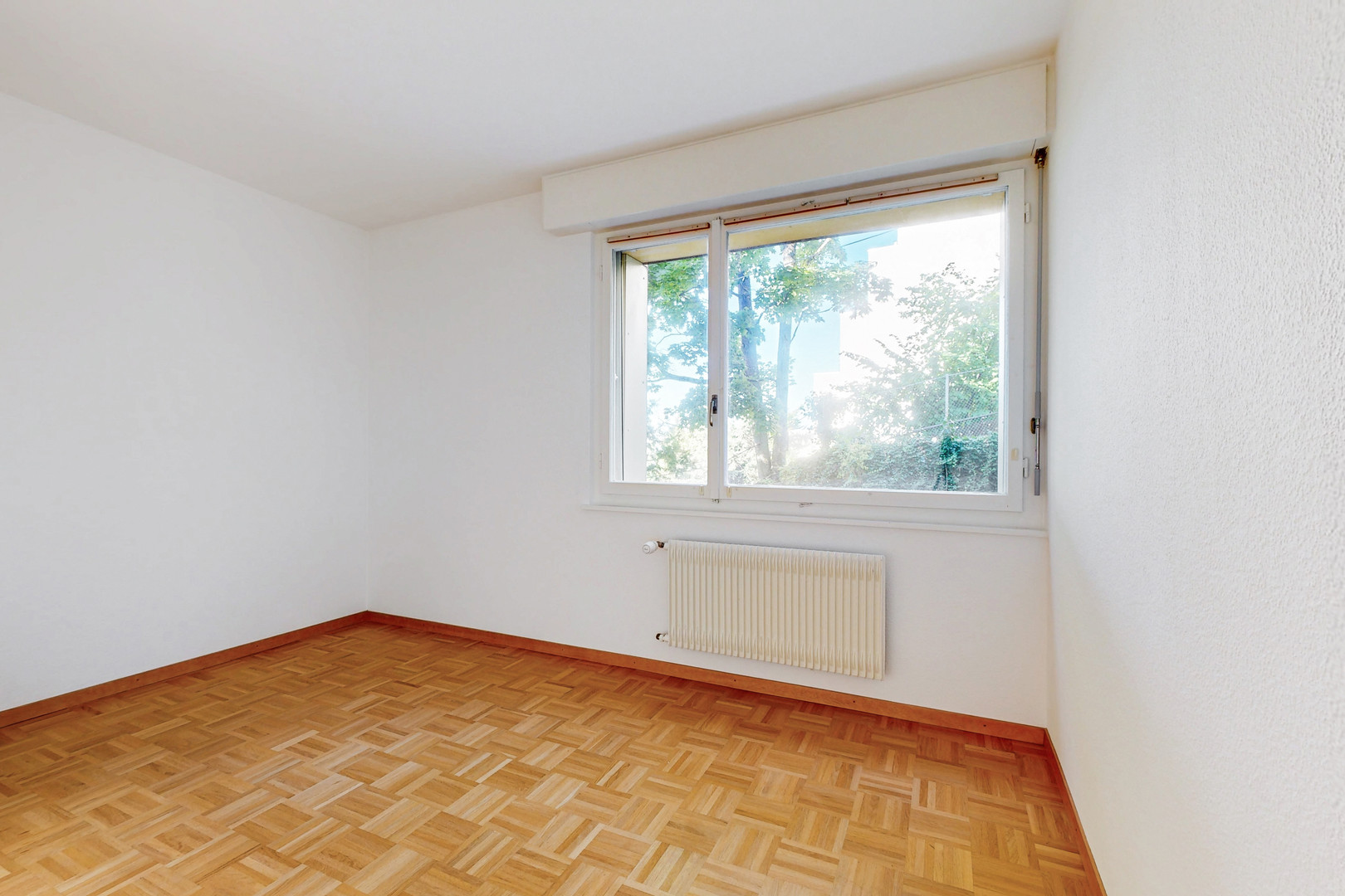 Leerer Wohnraum mit Parkett und Fenster