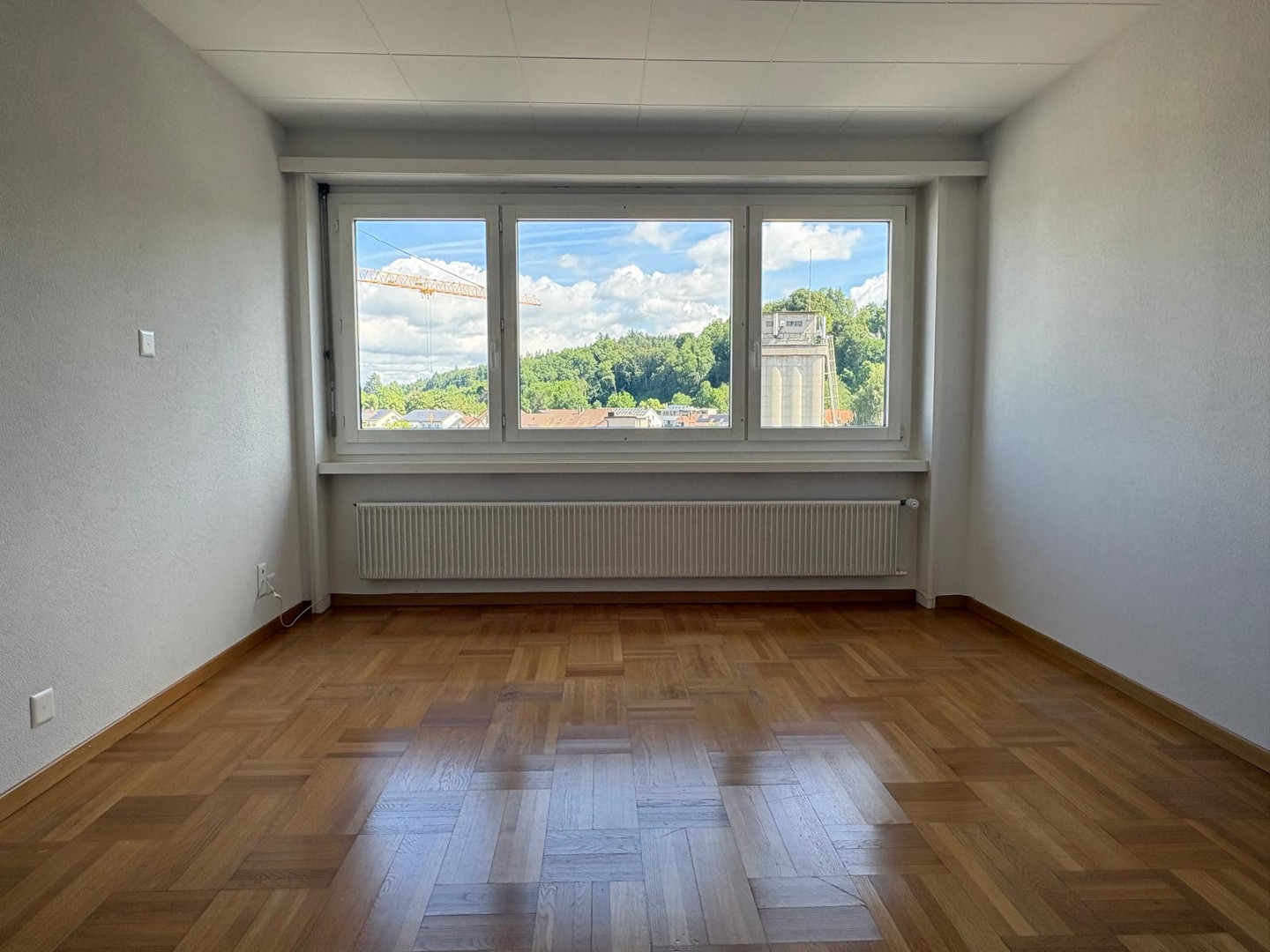 Leerer heller Raum mit großem Fenster und Parkettboden