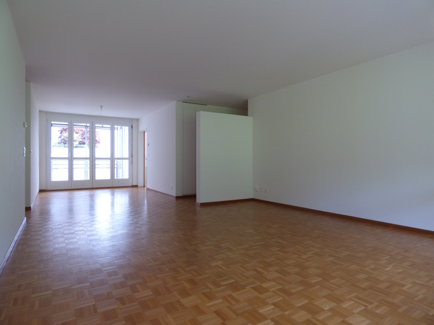 Leerer Wohnraum mit Parkett und großen Fenstern