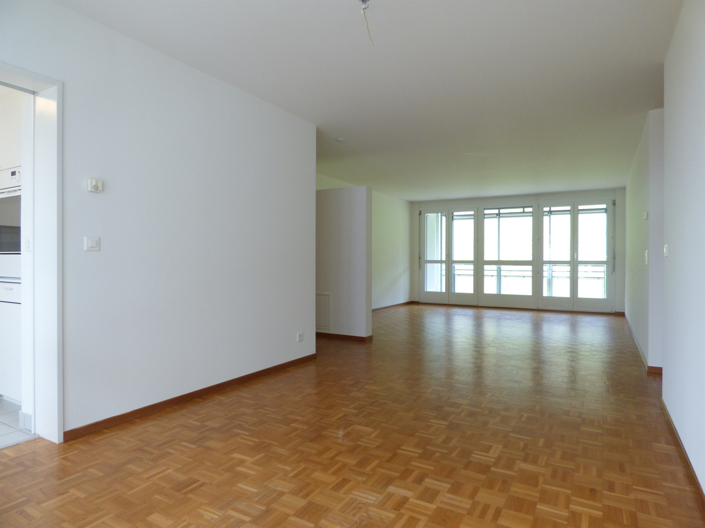 Heller, leerer Wohnraum mit Holzparkett und großen Fenstern