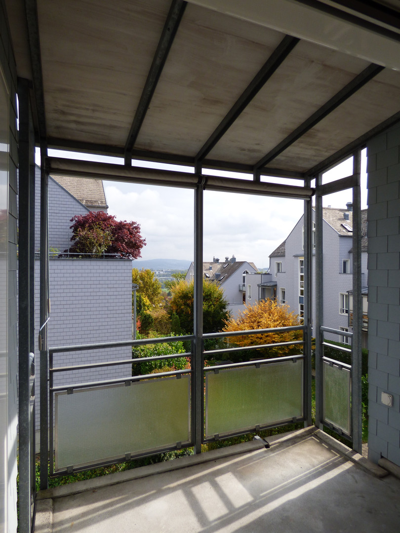Überdachter Balkon mit Blick auf Wohngebäude und Grün